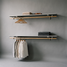 Two minimalist floating shelves mounted on a gray wall, styled with folded beige and dark gray textiles and light wood hangers, against a clean gray studio background.