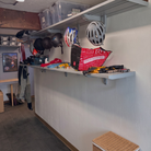 A wall-mounted bicycle storage system with two light gray shelves holding helmets, storage bins, and cycling accessories in a garage or shed setting.