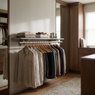 A wall-mounted clothing rack in a modern walk-in closet, holding multiple shirts on wooden hangers with folded textiles and decorative vases on a shelf above, set in warm wood cabinetry.