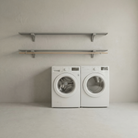 Toden gray modular laundry room storage system with a double-row shelf configuration. The setup features two 72-inch gray floating surfaces mounted above a white washer and dryer, with an integrated wooden closet rod for air-drying clothes. This visual highlights the sleek, no-diagonal support bracket design and the system's industrial-strength load capacity in a minimalist utility space.