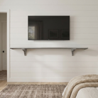 Toden gray modular surface installed as a minimalist floating TV console on a white shiplap wall. The 72-inch gray panel is mounted beneath a wall-mounted television, showcasing the heavy-duty brackets and sleek "no diagonal support" design. This setup demonstrates an industrial-strength media storage solution that doubles as a modern architectural feature in a bedroom or living area.