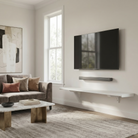 Toden white modular surface installed as a minimalist floating TV console base in a modern living room. The 72-inch white panel is mounted beneath a wall-mounted television and soundbar, highlighting the sleek, low-profile design and industrial-strength brackets. The setup showcases a clean, unobstructed wall space for a professional-grade media center.
