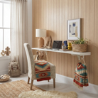 Toden white modular surface used as a minimalist floating desk in a modern home office with wood paneled walls. The long-run desk holds a laptop, lamp, and decor, while integrated white storage hooks organize headphones and a blanket. The setup showcases the "no diagonal support" design, providing maximum legroom and a clean, cable-free aesthetic for a professional workspace.