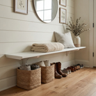 Toden white modular surface used as a floating entryway bench and shoe organizer in a modern mudroom. The heavy-duty white shelf is mounted on a white shiplap wall, styled with a knit blanket, pillow, and decorative vase. Below the bench, woven storage baskets and shoes are neatly arranged, showcasing the space-saving "no diagonal support" design of the brackets.
