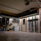 A garage interior with wall-mounted storage cubbies, a ski rack holding skis and snowboards, shelving, a chest freezer, and a bicycle wheel visible on the left.
