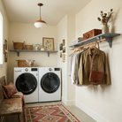 Toden gray modular laundry room storage system in a warm, modern utility space. A single gray floating shelf is mounted above the washer and dryer for basket storage, while a second gray shelf includes an integrated wooden closet rod for air-drying clothes and organizing outerwear. The setup showcases the industrial-strength brackets and sleek, no-diagonal support design for a cohesive home organization system.
