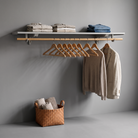 A wall-mounted clothing rack with a light wood rail and hangers, styled with folded neutral textiles and hanging garments against a gray wall.