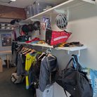 all-groups Toden white modular gear room system featuring a double-row shelving layout. The upper shelf uses integrated snap-fit hooks to organize multiple helmets and gear bags. The lower shelf includes a heavy-duty closet rod for hanging jerseys, jackets, and tactical vests. The setup demonstrates how the system maximizes vertical wall space for bulky athletic gear and apparel in a garage or mudroom setting.