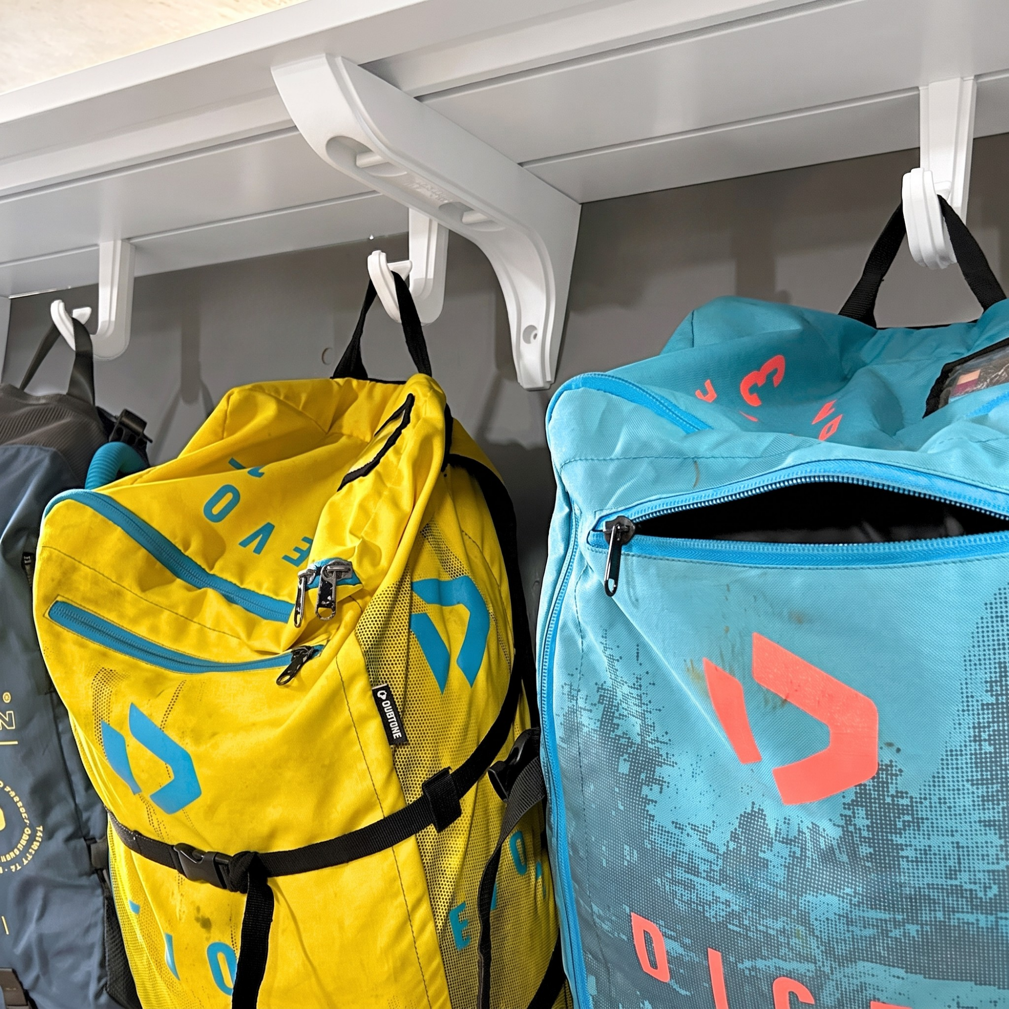 A bright yellow and a light blue DICKIE outdoor backpacks hanging from white wall hooks on a shelf. Bag hanging double hook is also great for all outdoor sports and beach equipment